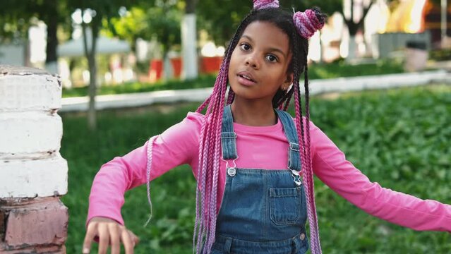 An African-American girl with pink braids acts like a doll on a city street.Slow motion.