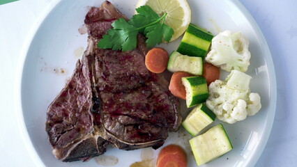 Juicy steak with legumes on plate, top view of meal of meat with cauliflower, carrots, zucchini. Delicious protein rich food