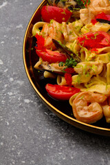 Pasta Spaghetti with mussels,fried prawns, tomatoes. On luxury black plate with gold lines.On grey marble.Copy space