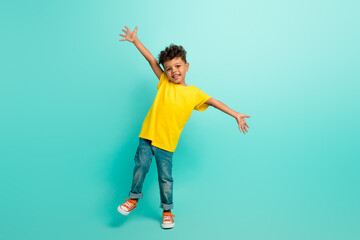 Full length photo of cheerful positive small boy with brown hair wear stylish t-shirt raising arms up isolated on teal color background