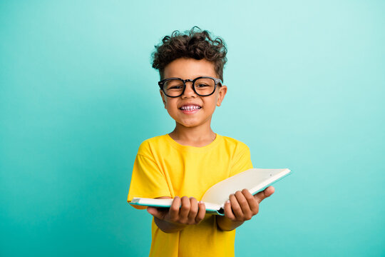 Portrait of smart small boy with brown hair wear stylish t-shirt in glasses hold book do homework isolated on teal color background