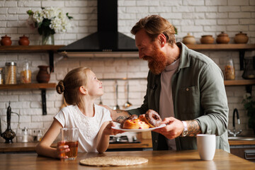 Happy tattooed father holding sweet pastry near freckled child during breakfast in morning