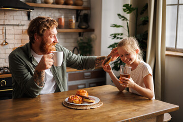 Smiling father touching hair of daughter with donut during breakfast in kitchen