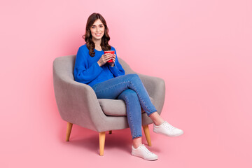 Obraz na płótnie Canvas Full size photo of lovely positive girl sit comfy soft chair hold coffee mug empty space isolated on pink color background