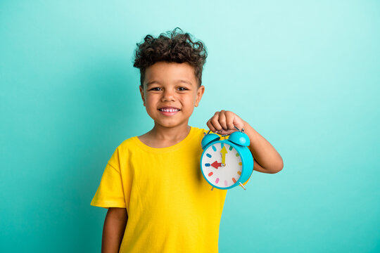 Portrait of good mood cheerful small boy with curly hairstyle wear stylish t-shirt hand holding clocks isolated on teal color background