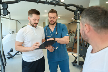 Physiotherapist and gym trainer discussing exercise program for patient