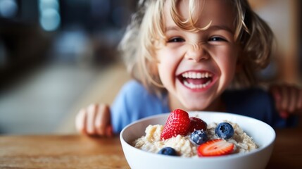 Smiling adorable child having breakfast eating oatmeal porridge with berries. 