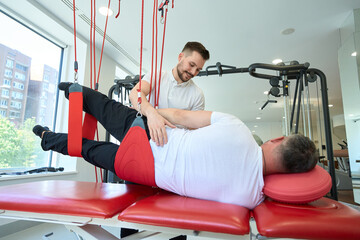 Professional kinesiotherapist rehabilitating patient using gym equipment