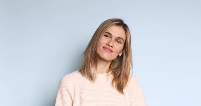 Friendly looking positive straight hair woman blonde haircut shows shaka sign gestures indoor being in high spirit, wears fashionable sweater isolated on blue background. Girl show hi or hello gesture