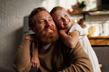 Portrait of smiling freckled girl and bearded father looking away together at home, parenthood...