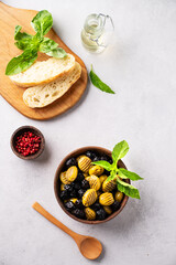 A set of green and black dried olives in wooden bowl  with fresh chiabatta bread on a light background with olive oil and basil. The concept of vegetarian healthy snacks.