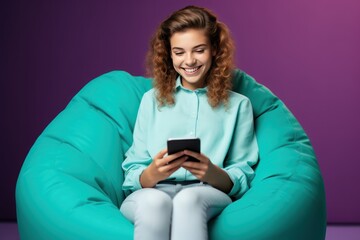 smiling young woman using smartphone in bean bag chair isolated on violet. Business Concept. Coworker. Freelance Concept. Office Concept with Copy Space.