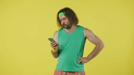 Man in green top and headband reading something on his smartphone. Isolated on yellow background.