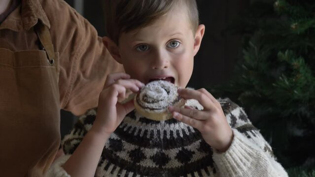 Little boy in sweater eating Christmas sweden cinnamon bun at home