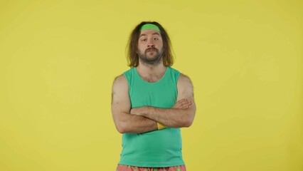 Man in green top and headband standing and looking with crossed arms. Isolated on yellow background.