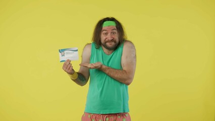Man in green top and headband advertises sports gift certificate, smiling, pointing. Isolated on yellow background.