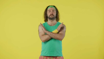 Man in green top and headband showing negative no sign with crossed hands. Isolated on yellow...