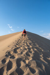 Woman climbing a large sand dune at sunset