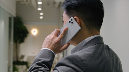 Back view Asian businessman speak in office hallway male middle-aged professional entrepreneur chinese korean man talk mobile phone business discussion negotiation turn head converse tell communicate