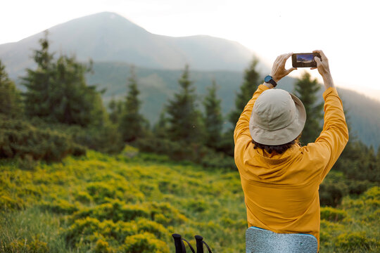 the traveler takes a photo on the phone against the background of mountain landscapes. A tourist is looking for a mobile connection or mobile phone network signal in the mountains