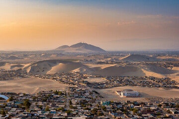 The sun sets over a city in Peru surrounded by sand dunes at sunset.