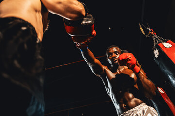 African American Black boxer punching at trainer or coach wearing punching mitts as boxing bag training equipment in the gym. Strength and stamina training for professional boxing match. Impetus