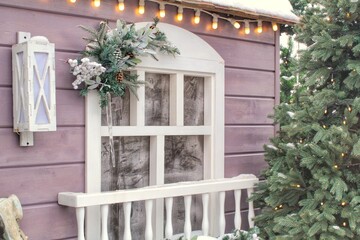 Frosted window sill with christmas decoration. Winter holiday home, view from outdoors. Fir tree garland on wooden board of front yard facade house. New Year festive decor of the streets