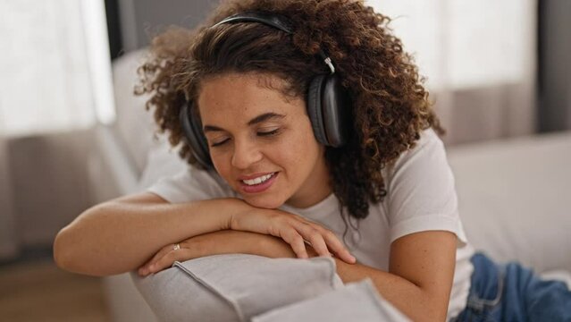 Young beautiful hispanic woman listening to music relaxed on sofa at home