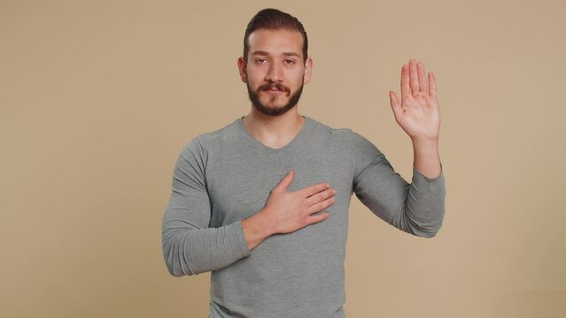 I swear to be honest. Sincere responsible lebanese young man raising hand to take oath, promising to be honest and to tell truth, keeping hand on chest. Middle eastern guy isolated on beige background
