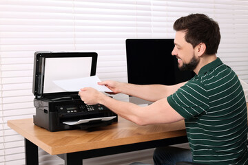 Man using modern printer at wooden table indoors