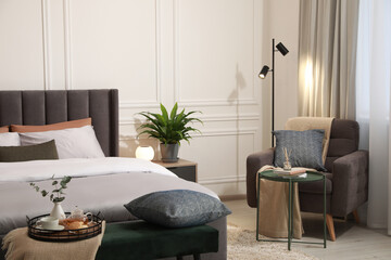 Stylish bedroom interior with large comfortable bed, armchair and ottoman