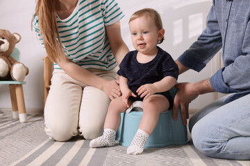 Parents training their child to sit on baby potty indoors