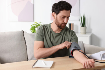 Man measuring blood pressure at wooden table in room