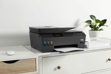 Modern printer with paper on chest of drawers indoors