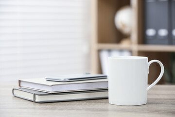 White ceramic mug and notebooks on wooden table indoors. Space for text