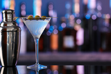 Martini glass with cocktail and shaker on counter in bar. Space for text