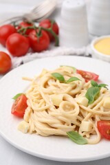 Delicious pasta with brie cheese, tomatoes and basil leaves on white table, closeup