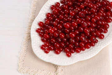 Plate with ripe red currants on white wooden table, top view