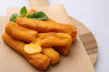 Tasty fried mozzarella sticks and basil on light table, closeup