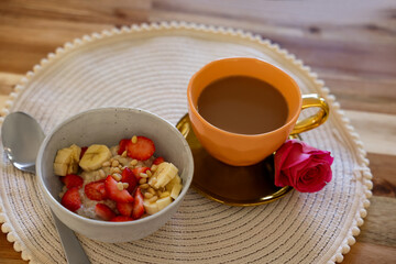 Delicious oatmeal with banana, strawberries, nuts and cup of hot drink on wooden table