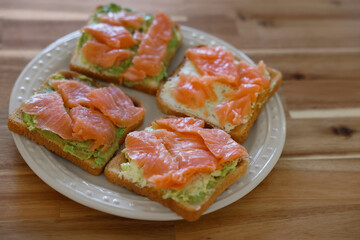 Sandwiches with avocado spread and salmon on wooden table, closeup