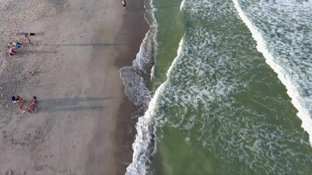 aerial footage along the Atlantic coastline at Kure Beach with people relaxing on the beach, blue ocean water, waves, green grass, trees and homes along the coast in Wilmington North Carolina USA