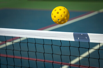 Yellow Pickleball crossing a Pickleball net with shadow on the top tape.