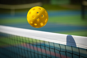 Yellow Pickleball crossing a Pickleball net with shadow on the top tape.