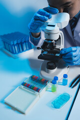 Asian scientist looking at a microscopic sample of experimental cyan is doing an in vitro vaccine experiment in a science lab. medical research concept.