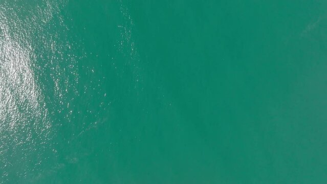 A drone starts pointing downward, showcasing a marvellous blue sea, gradually moving forward to reveal a paradisaical coastline on the coast of Brazil, in 4k. Paradise is here