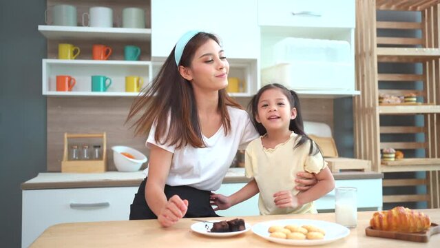 Happy cheerful Asian woman and her lovely little daughter living together in kitchen, mother embracing and hugging daughter. Single mom concept.