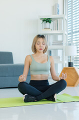 Fototapeta na wymiar Asian young fit female teenager in sportswear sport bra legging sneakers sitting closed eyes meditating on yoga mat with lotus posture exercising training together in living room at home.