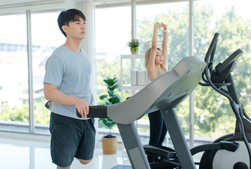 Asian young fit male female athlete jogger runner in sportswear sport bra legging wear wireless headphones smiling holding hands high five while exercise training on treadmill and elliptical machine