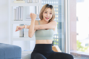 Fototapeta na wymiar Asian young sexy pretty fit female athlete teenager in sportswear sport bra leggings and watch sitting smiling stretching arms and hands on exercise ball warming up working out in living room at home
